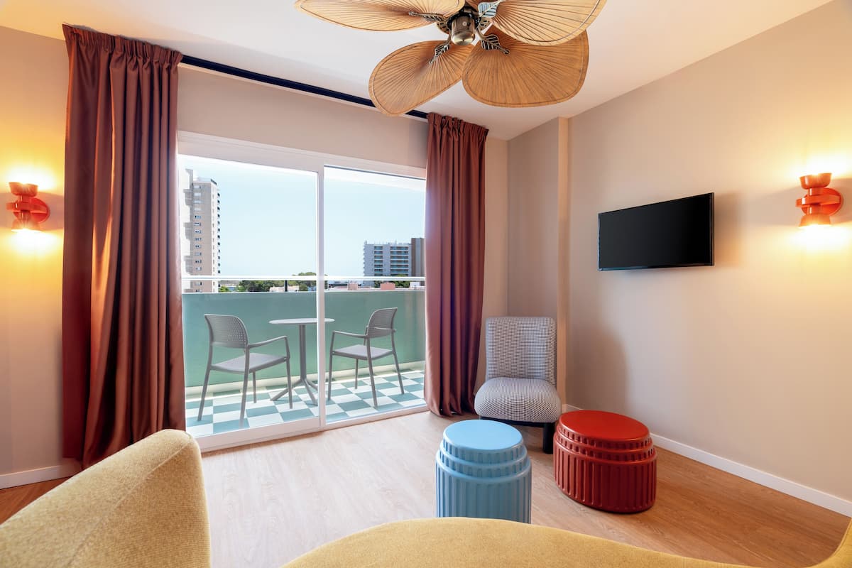 A modern hotel room with a balcony, a flat-screen TV, and a ceiling fan.