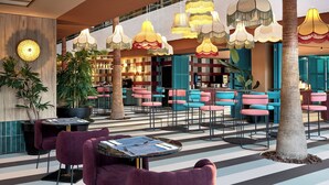 A modern indoor area with striped flooring, multiple seating areas with tables, and hanging decorative lamps. - tent Mojito Suites (Calvia)