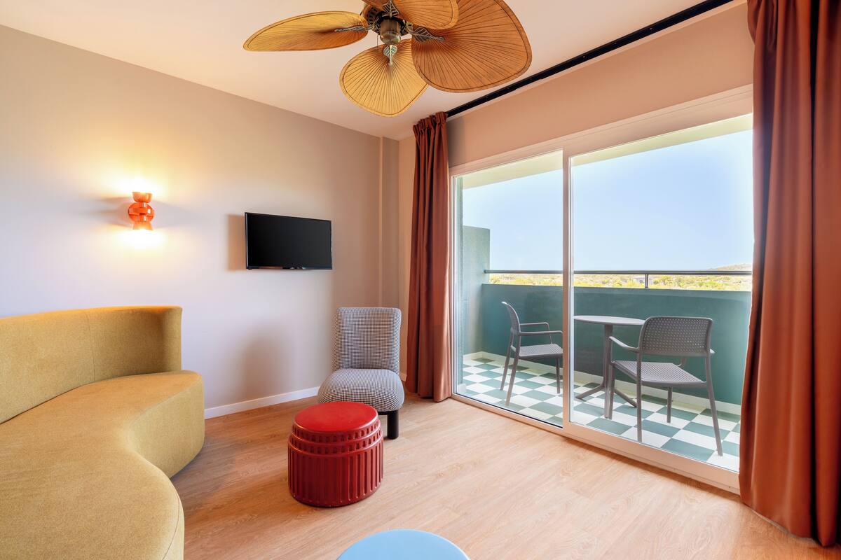 A modern room with a sofa, ottoman, and chairs near a balcony with a checkered floor.