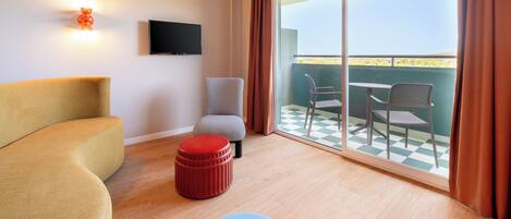 A modern room with a sofa, ottoman, and chairs near a balcony with a checkered floor.