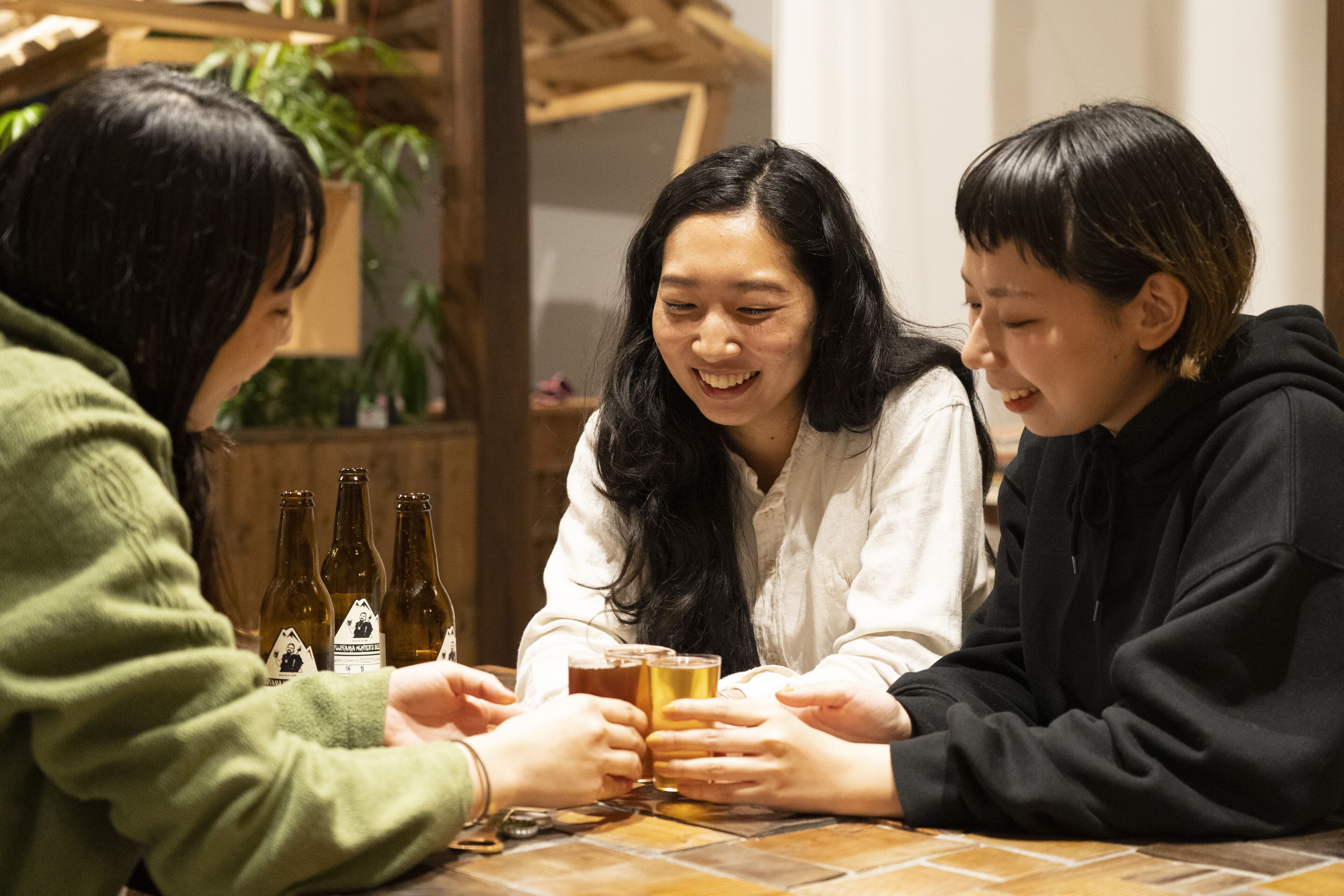 Trois personnes sont assises à une table, devant des bouteilles de bière et des verres.
