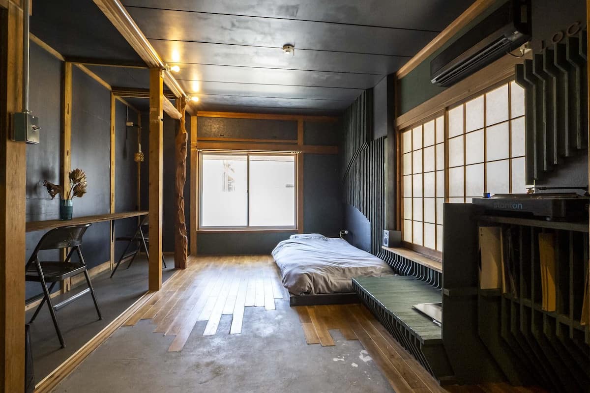 Ein kleines Zimmer mit einem Bett, einem Sessel, einer Heizung und einem großen Fenster.