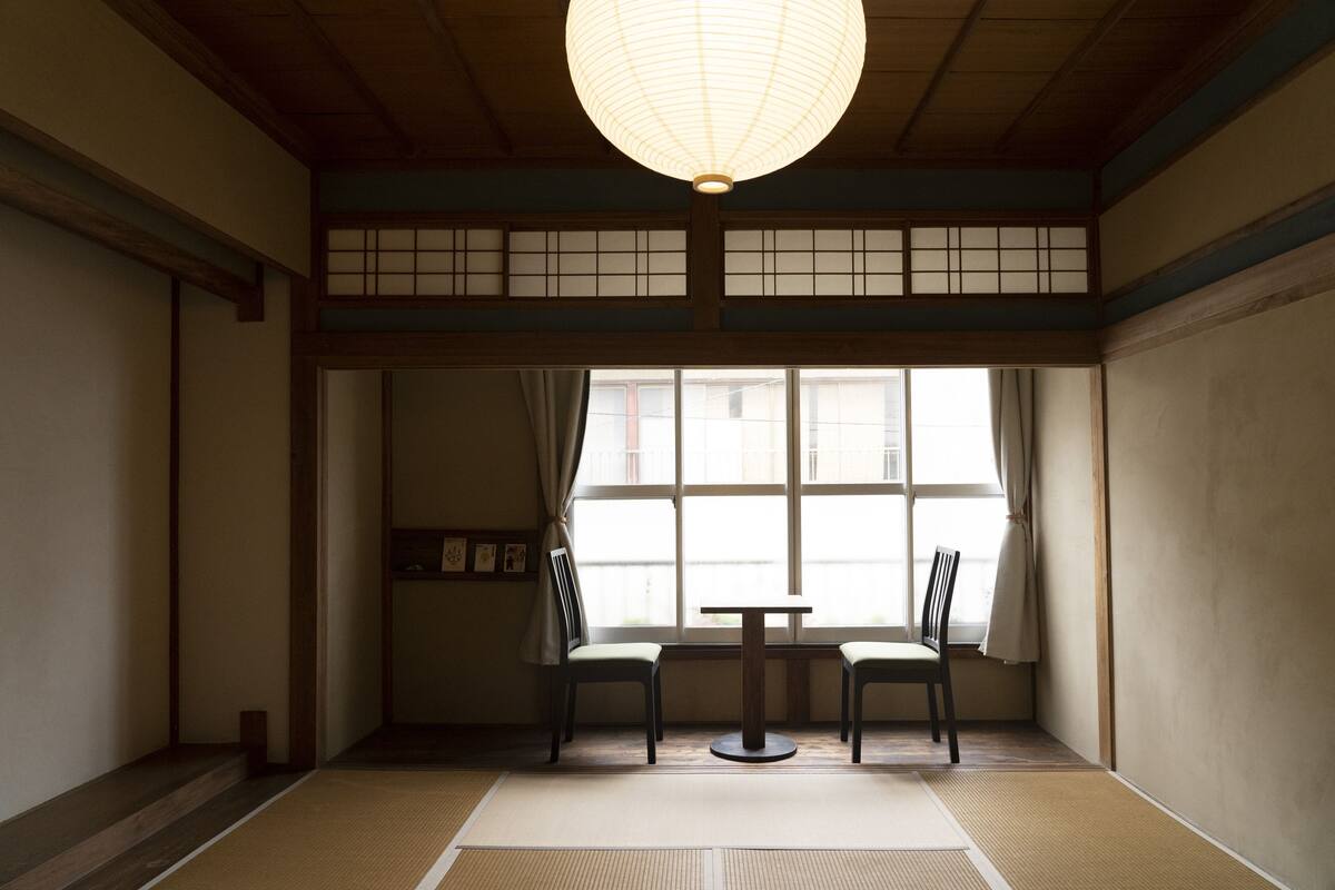 Ein traditioneller japanischer Raum mit Tatami-Böden, einem niedrigen Tisch, zwei Stühlen und einer Shoji-Schiebetür.