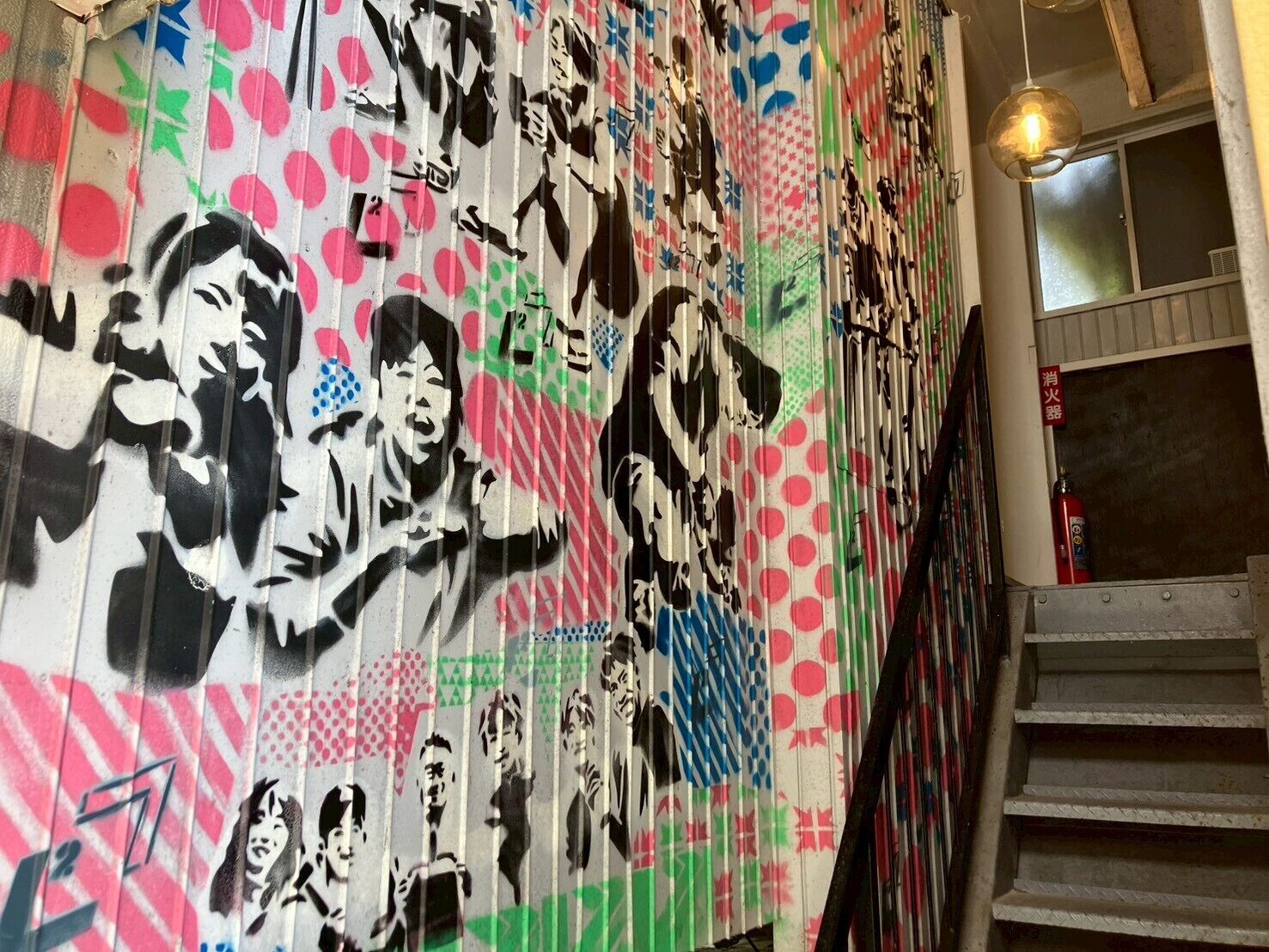 Una escalera con un muro que presenta un colorido mural con diversos diseños abstractos y figurativos.