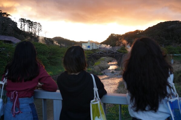 Tres personas mirando un río, con un puente y un edificio al fondo.