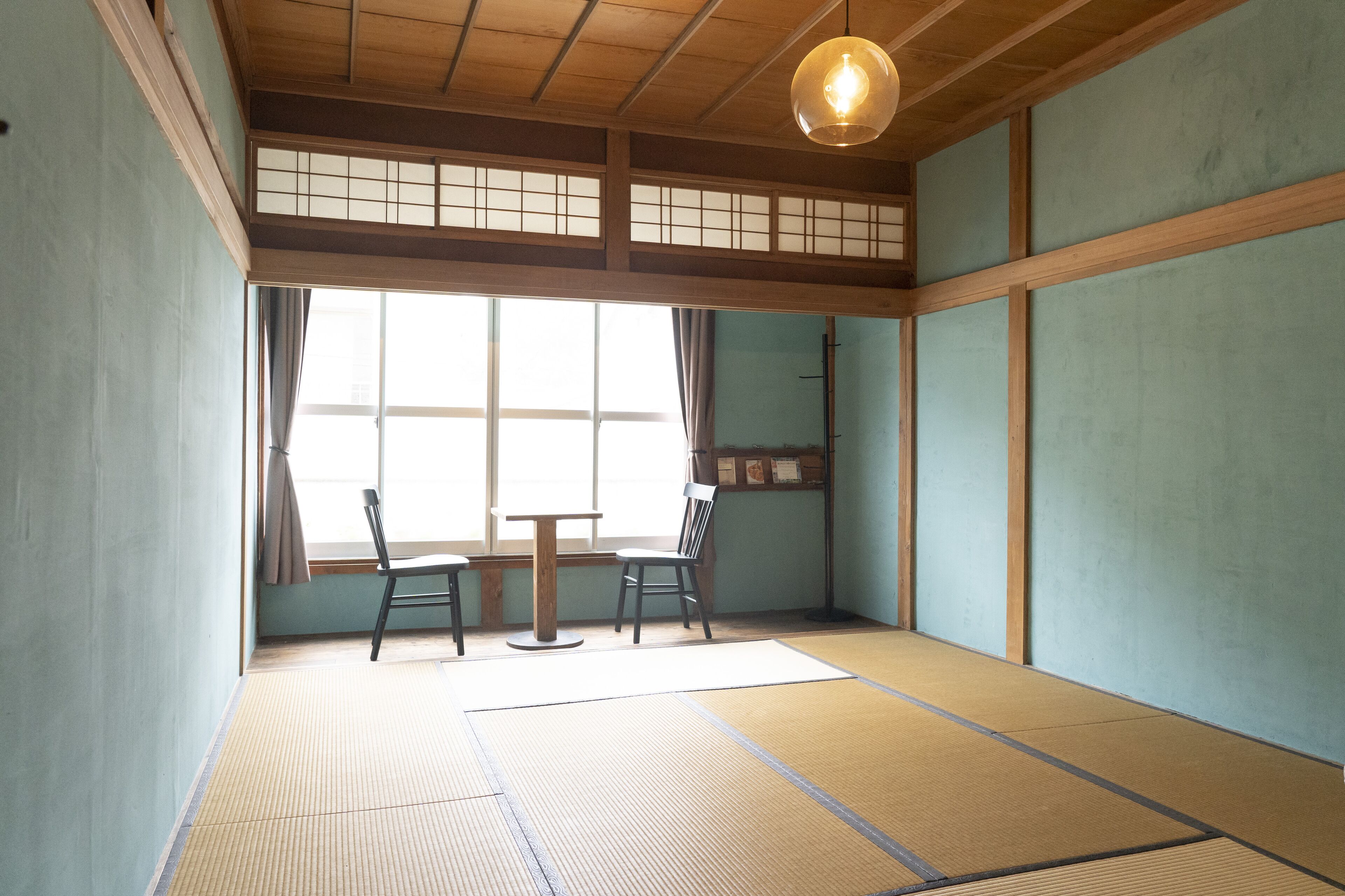 Una habitación japonesa tradicional con suelo de tatami, una mesa de madera baja, dos sillas y una ventana con celosías shoji.
