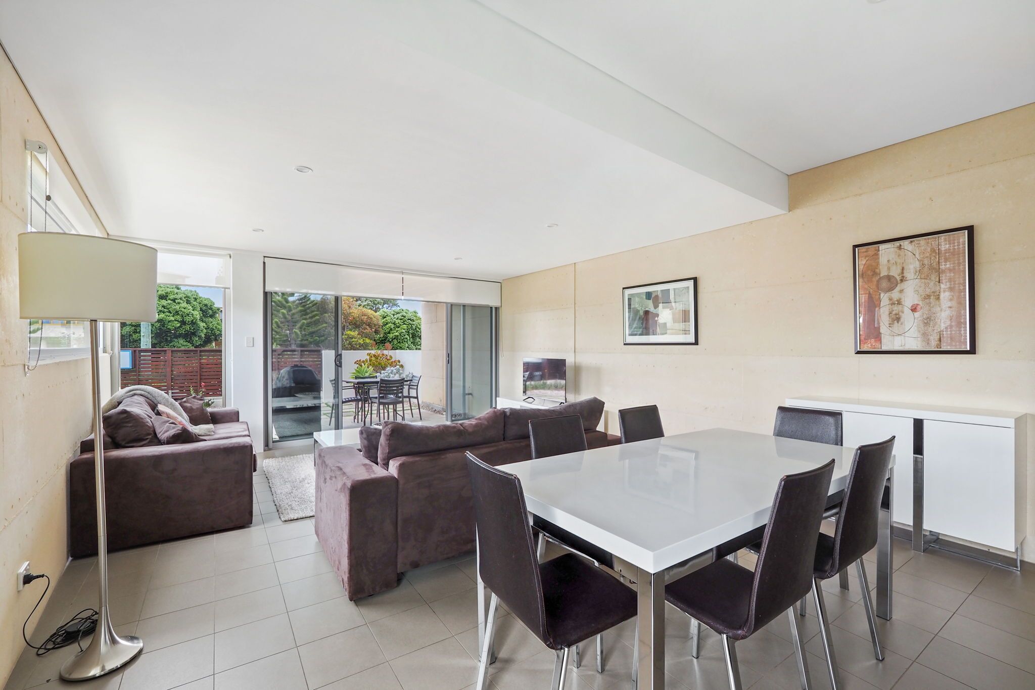 Un salon moderne avec un coin repas, comprenant un ensemble de canapés, une table à manger avec des chaises, un lampadaire et une grande fenêtre offrant une vue sur l’extérieur.