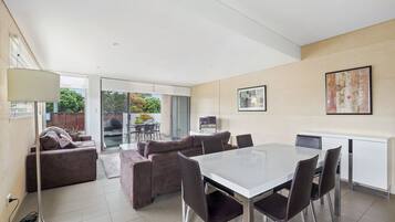 Un salon moderne avec un coin repas, comprenant un ensemble de canapés, une table à manger avec des chaises, un lampadaire et une grande fenêtre offrant une vue sur l’extérieur.