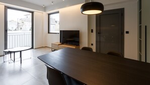 Ein modernes Wohnzimmer mit einem großen Holztisch, einem Fernseher und einem Balkon mit Blick auf Gebäude.