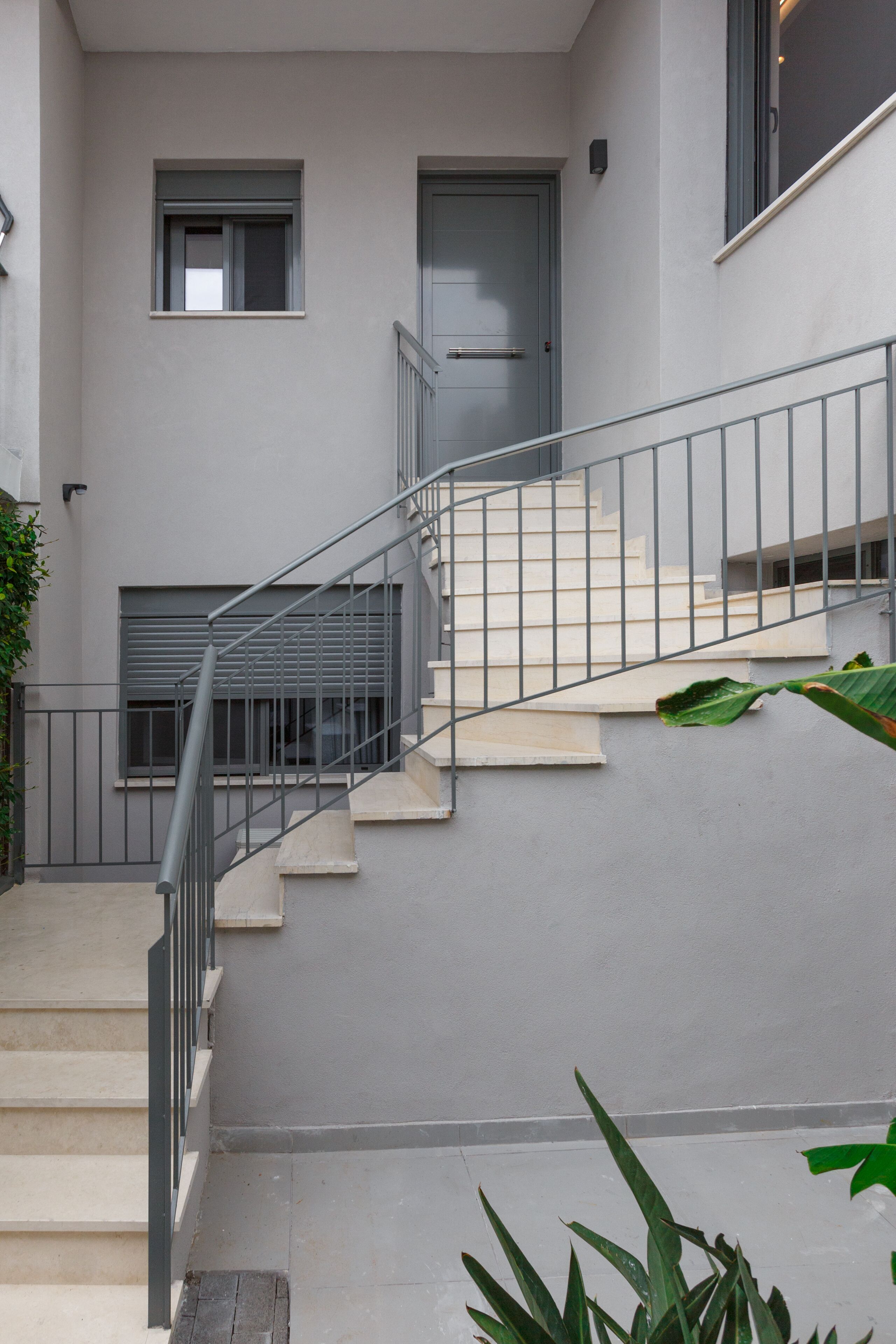 A modern building with a grey exterior, a staircase with metal railings, and a door with a window above it.