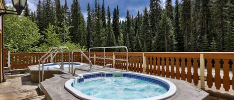 A hot tub with a wooden deck and a railing, surrounded by a forest.