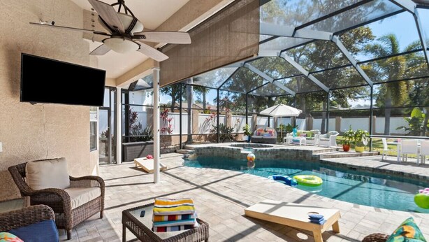 An indoor pool area with wicker furniture, a ceiling fan, and a TV mounted on the wall.