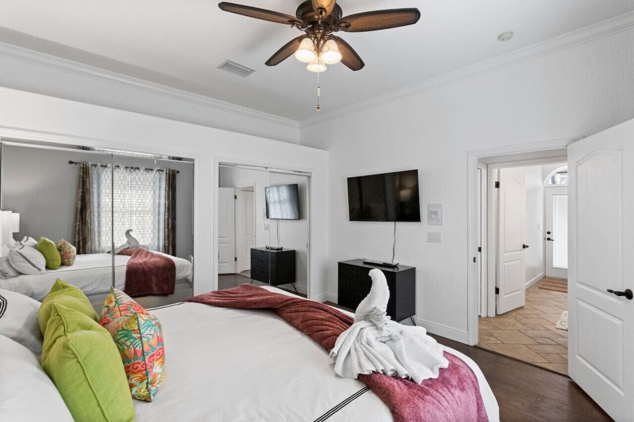 A hotel room with a large bed, a ceiling fan, a flat-screen TV, and a mirror.