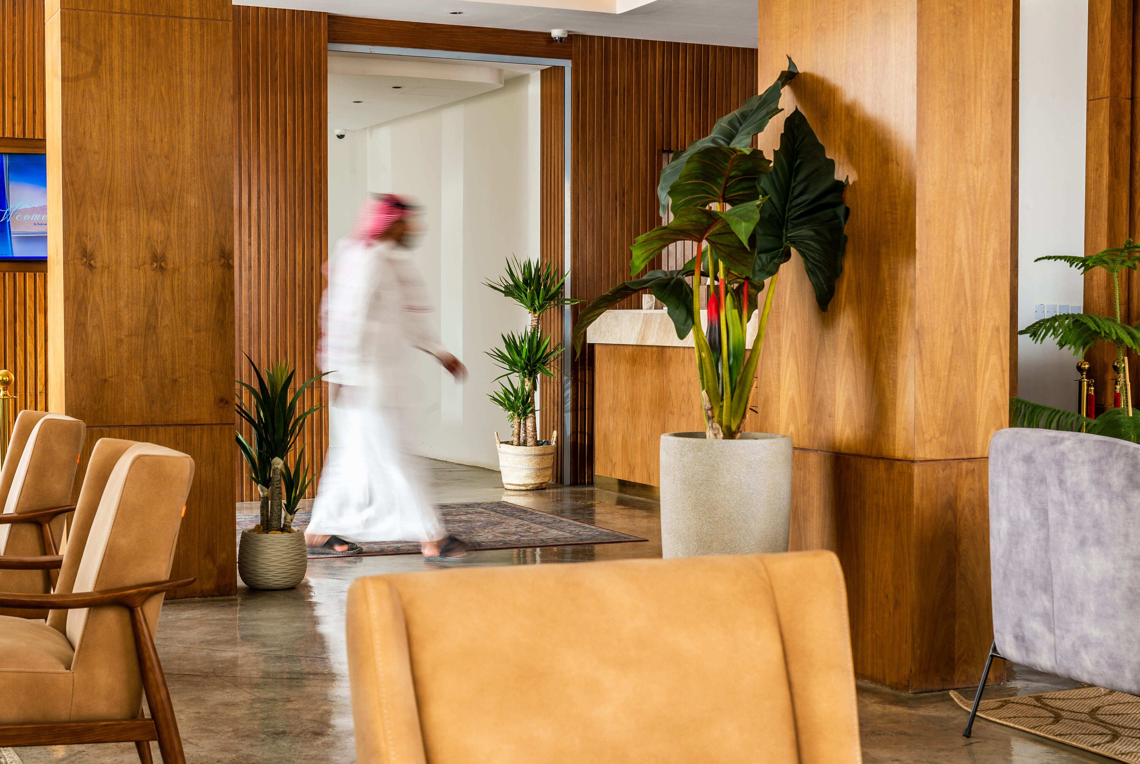 Un hall de hotel con paneles de madera, mostrador de recepción, varias sillas y plantas en macetas.