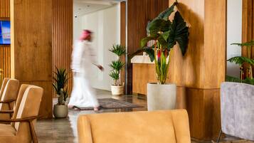 Un hall de hotel con paneles de madera, mostrador de recepción, varias sillas y plantas en macetas.