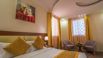 A hotel room with a bed, two armchairs, a small table with a vase of flowers, and a painting on the wall.