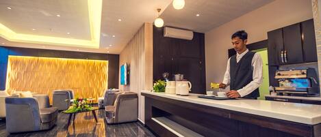 A modern hotel lobby with seating, a reception desk, and a coffee machine.