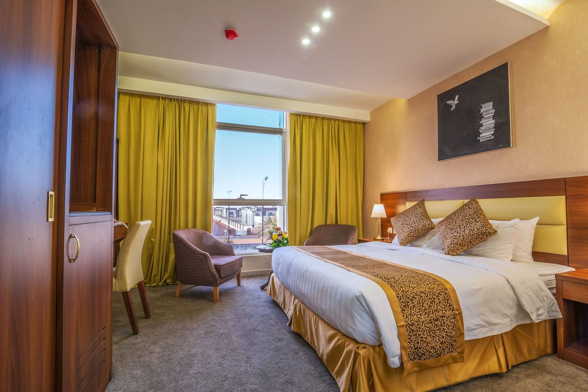 Una habitación de hotel con una cama grande, dos sillas, un escritorio y una ventana con cortinas.
