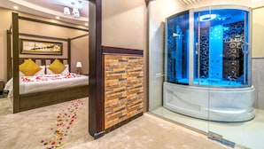 A bedroom with a four-poster bed, a glass-enclosed steam room, and a shower with a glass door. - Suknai Aja Serviced apartments (Ha'il)