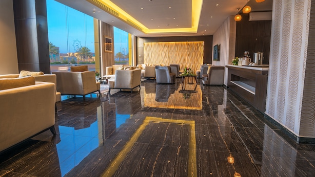 A modern hotel lobby with a polished marble floor, comfortable seating, a reception desk, and large windows offering a view of palm trees. - Suknai Aja Serviced apartments (Ha'il)