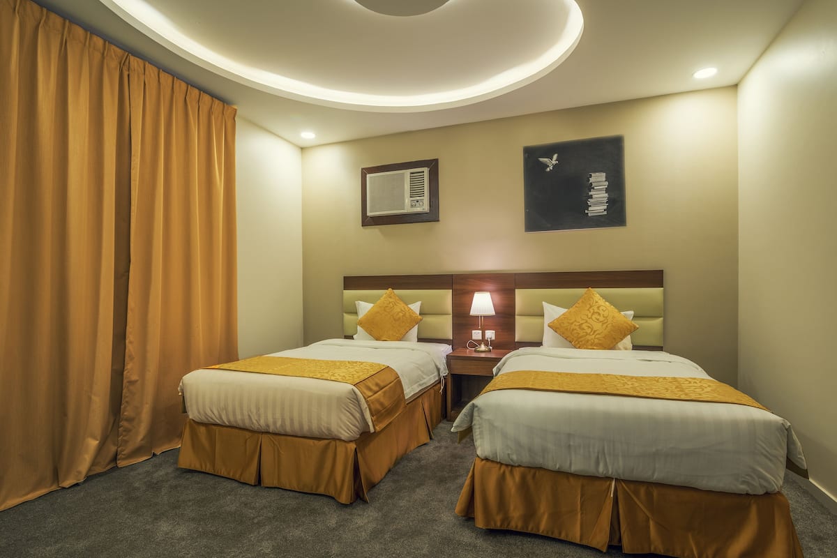 Habitación de hotel con dos camas, una mesita de noche con lámpara, aire acondicionado de pared y un cuadro con un pájaro.
