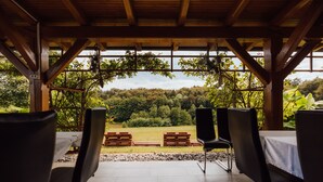 Un espace extérieur abrité, doté de poutres en bois et offrant une vue sur un paysage boisé.