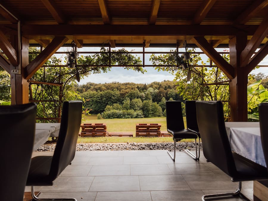 A covered outdoor seating area with wooden beams and a view of a forested landscape.