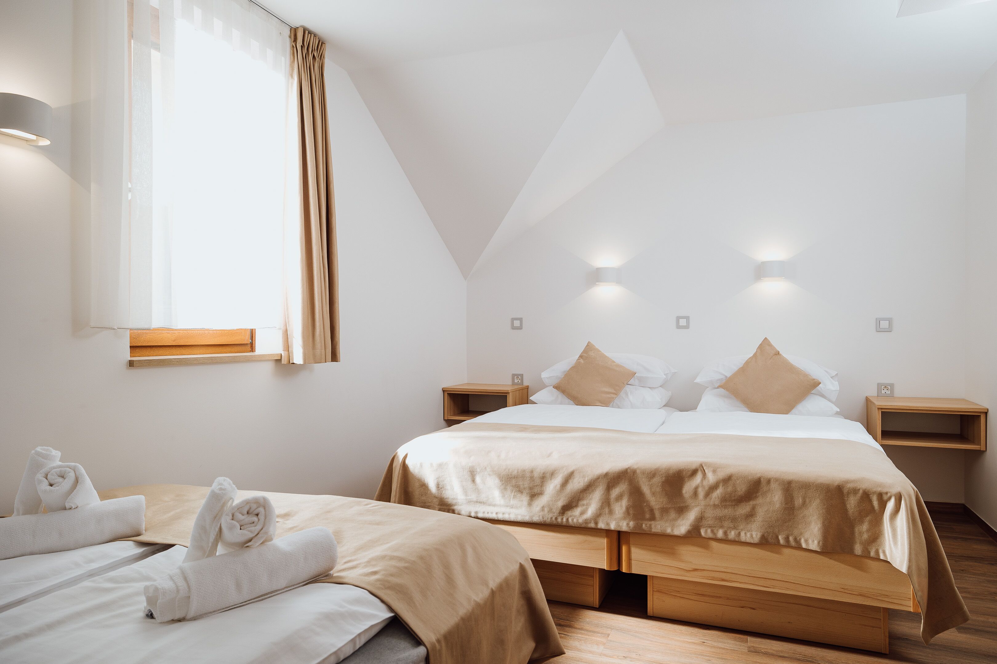 A modern hotel room with a large bed, two bedside tables, a wooden floor, and a window with curtains.