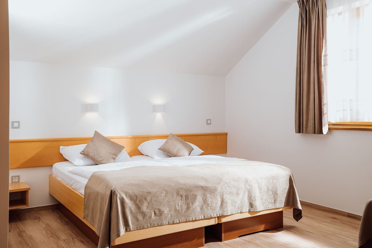 Una cama bien hecha con tablero de madera, una mesita de noche y una ventana con cortinas.