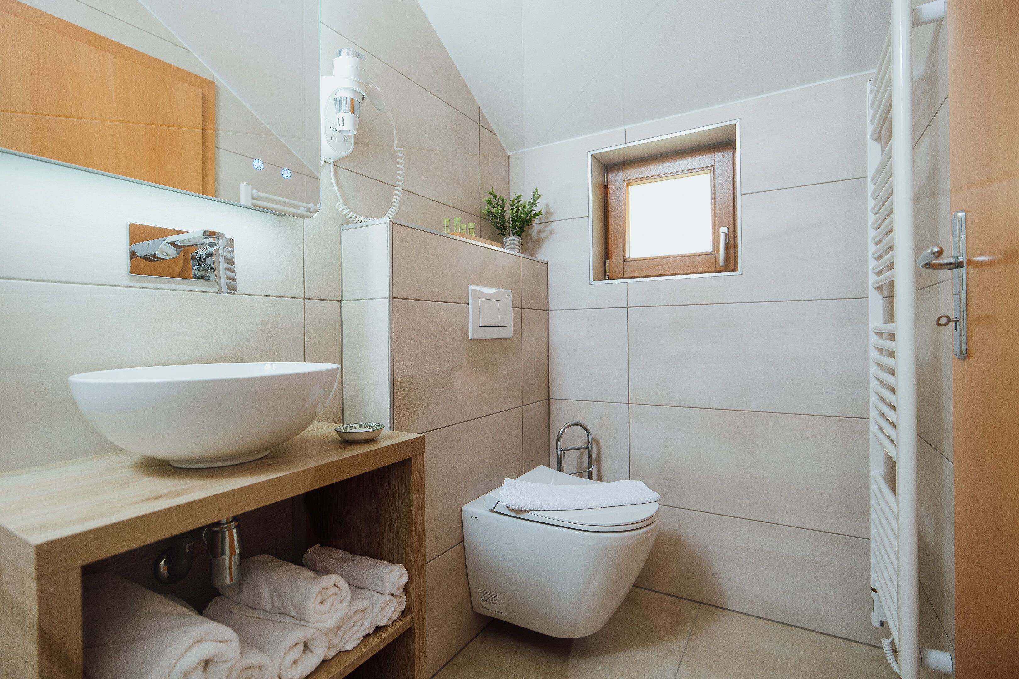 Un baño moderno con un lavamanos grande de color blanco, un inodoro y una ventana pequeña.