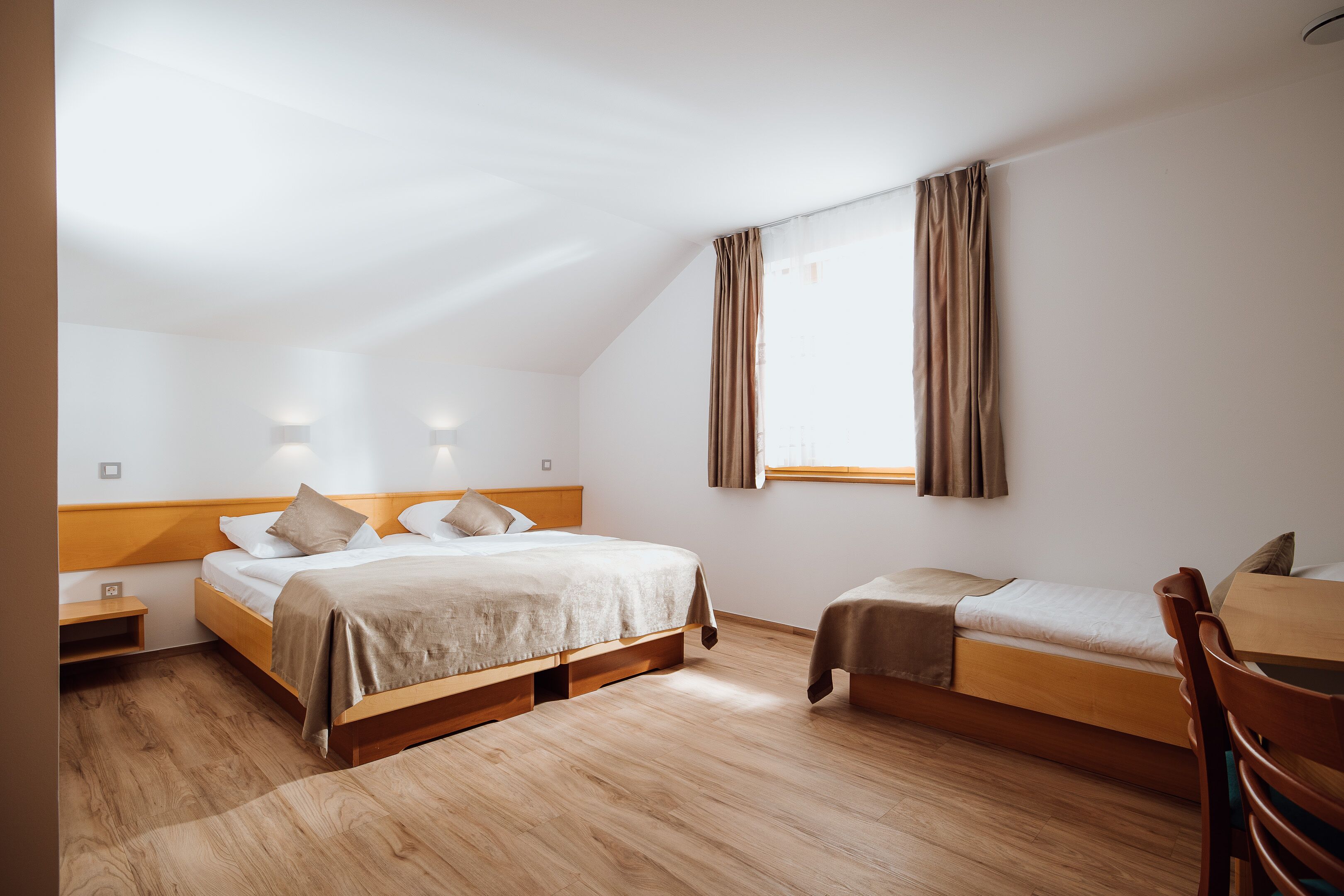 A room with a large bed, a smaller bed, a desk, and a chair.