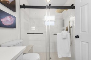 A modern bathroom with a glass shower enclosure, a toilet, a sink, and a towel rack.