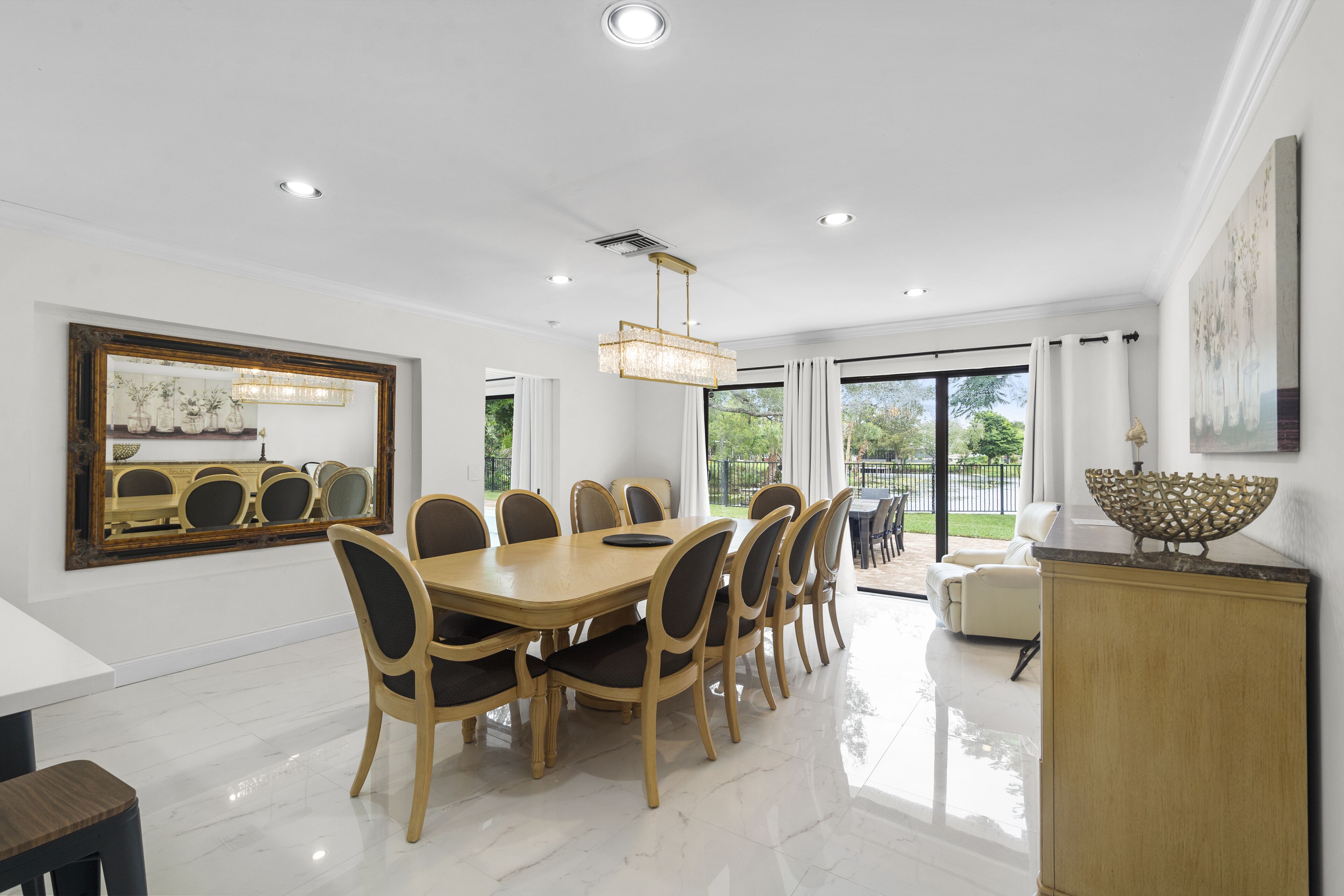 A spacious dining area with a large wooden table and chairs, a chandelier, and a view of the outdoors.