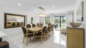 A spacious dining area with a large wooden table and chairs, a chandelier, and a view of the outdoors.
