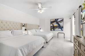 A modern bedroom with two beds, a ceiling fan, and a large abstract painting.