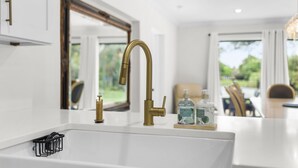 A modern kitchen with a gold faucet, white cabinetry, and a view of the outdoors.