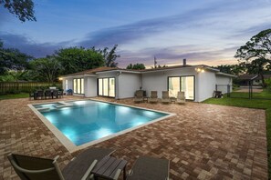 A modern house with a swimming pool, patio furniture, and a well-maintained lawn.