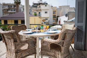 A round table with wicker chairs on a balcony overlooking a cityscape.