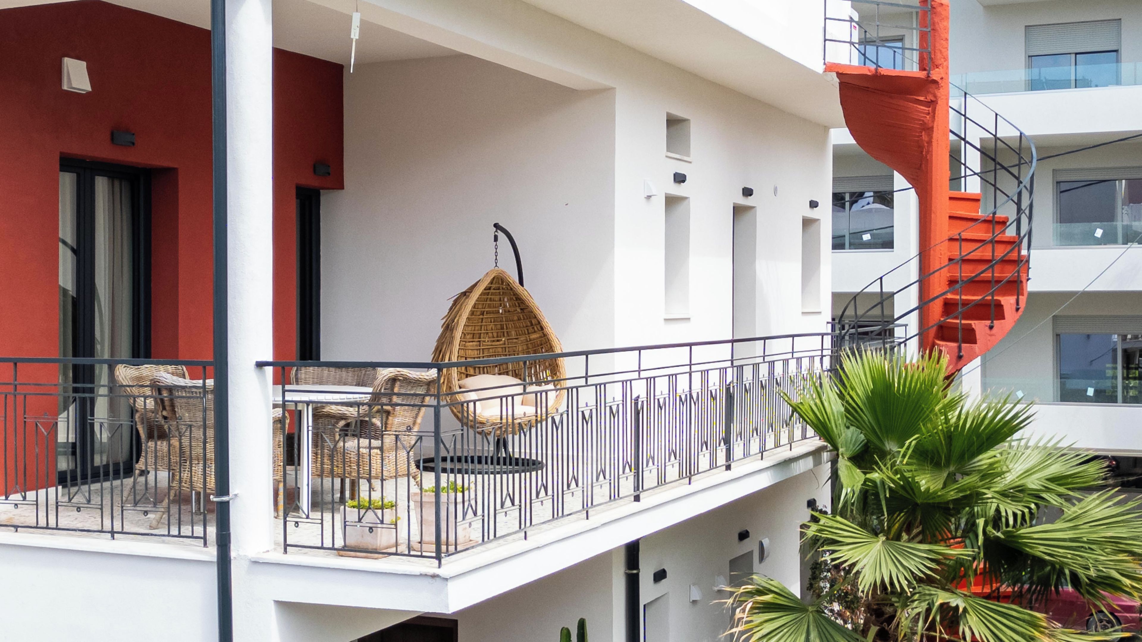 Un balcone con mobili in vimini, una sedia a dondolo e una scala a chiocciola rossa.