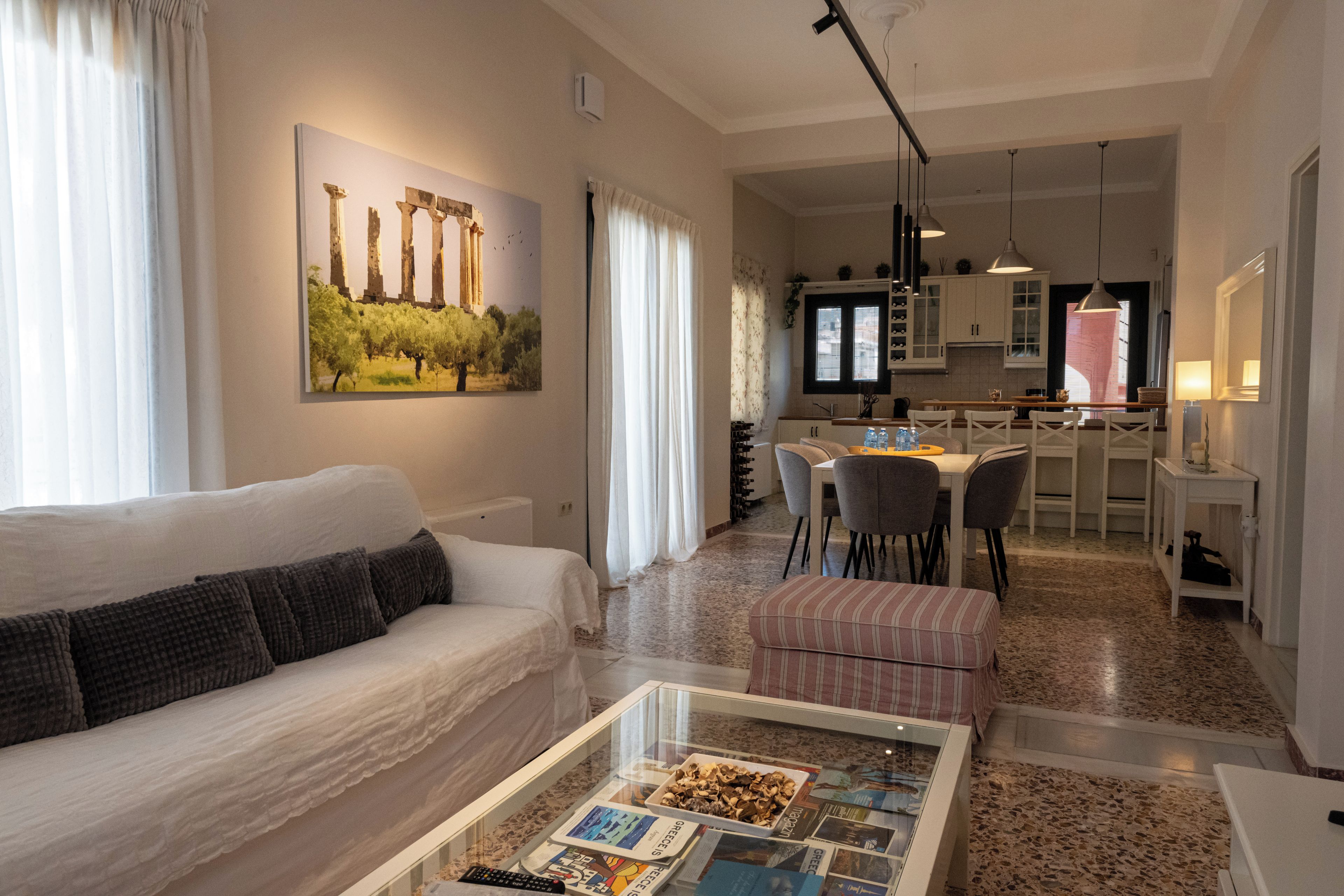 Ein modernes Wohnzimmer mit einer Couch, einem Couchtisch mit Zeitschriften, einem Essbereich mit Stühlen und einer Küche im Hintergrund.