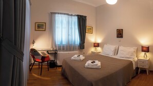 Habitació d'hotel amb llit, taules de nit, escriptori, cadira i finestra amb cortines.