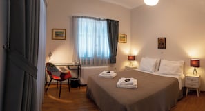 A hotel room with a bed, bedside tables, a desk, a chair, and a window with curtains.