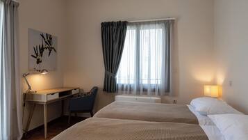 Habitación de hotel con dos camas, un escritorio, una silla y una ventana con cortinas.