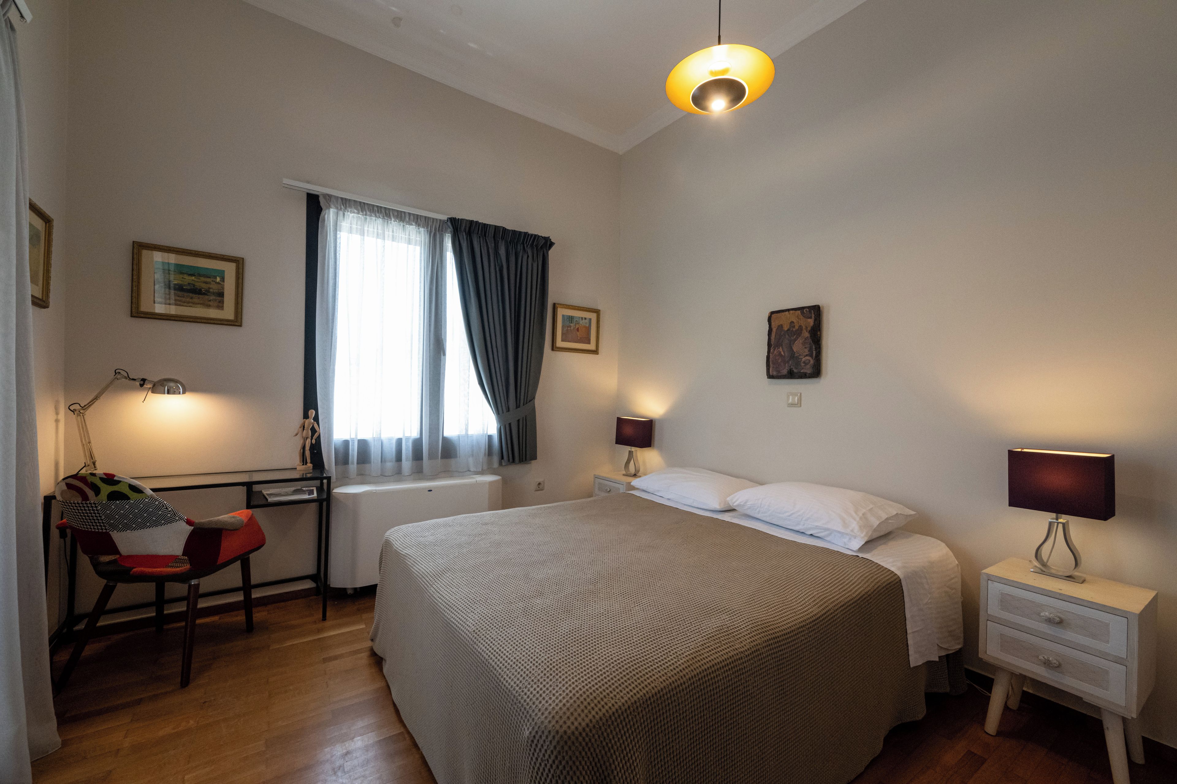 Ein Schlafzimmer mit einem großen Bett, einem Schreibtisch mit Stuhl, einem Fenster mit Vorhängen und zwei Nachttischlampen.