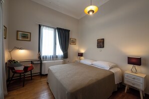 A bedroom with a large bed, a desk with a chair, a window with curtains, and two bedside lamps.