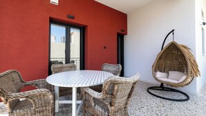 A round table with wicker chairs, a hanging chair, and a red wall with a window. - Angelinas Quarters - Kalamata Mediterranean Villas
 (Kalamata)