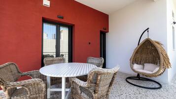 A round table with wicker chairs, a hanging chair, and a red wall with a window.