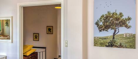 A hallway with a framed picture of a tree and birds, a staircase with a yellow cushion, and a white door.