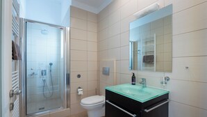 Un bany modern amb una cabina de dutxa de vidre, un vàter blanc i un moble de bany negre amb un lavabo de vidre.