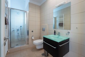 A modern bathroom with a glass shower enclosure, a white toilet, and a black vanity with a glass sink.